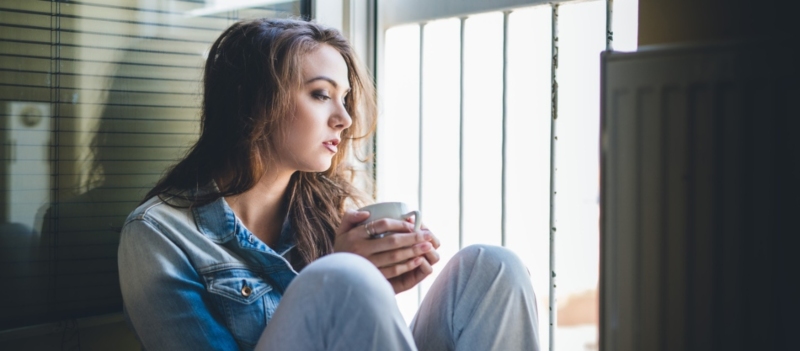 A stock image of woman holding coffee cup looking out window